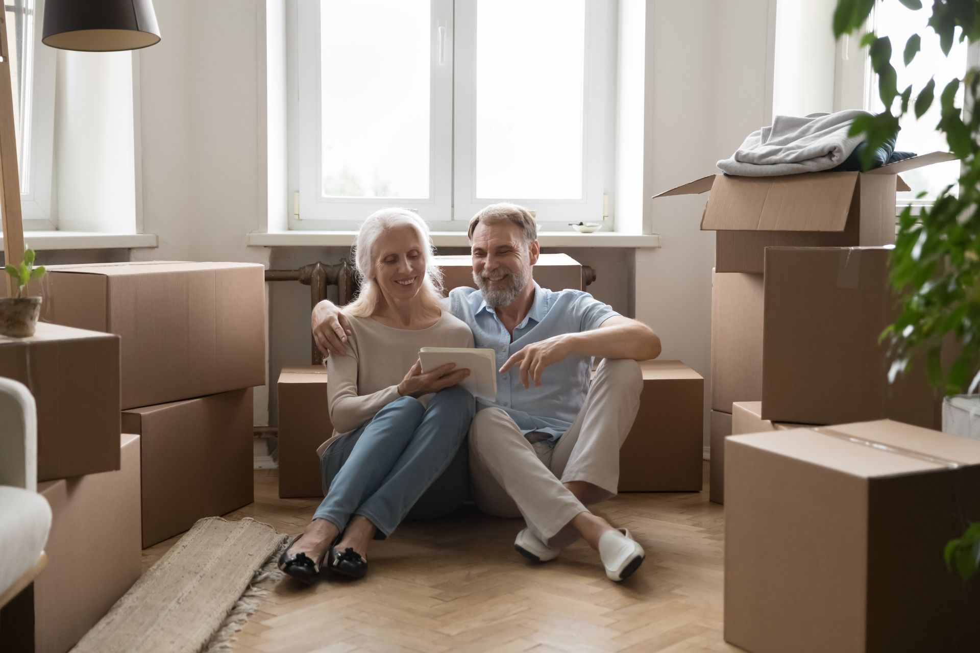 Couple sitting on the floor among moving boxes in a bright apartment, reviewing a list together