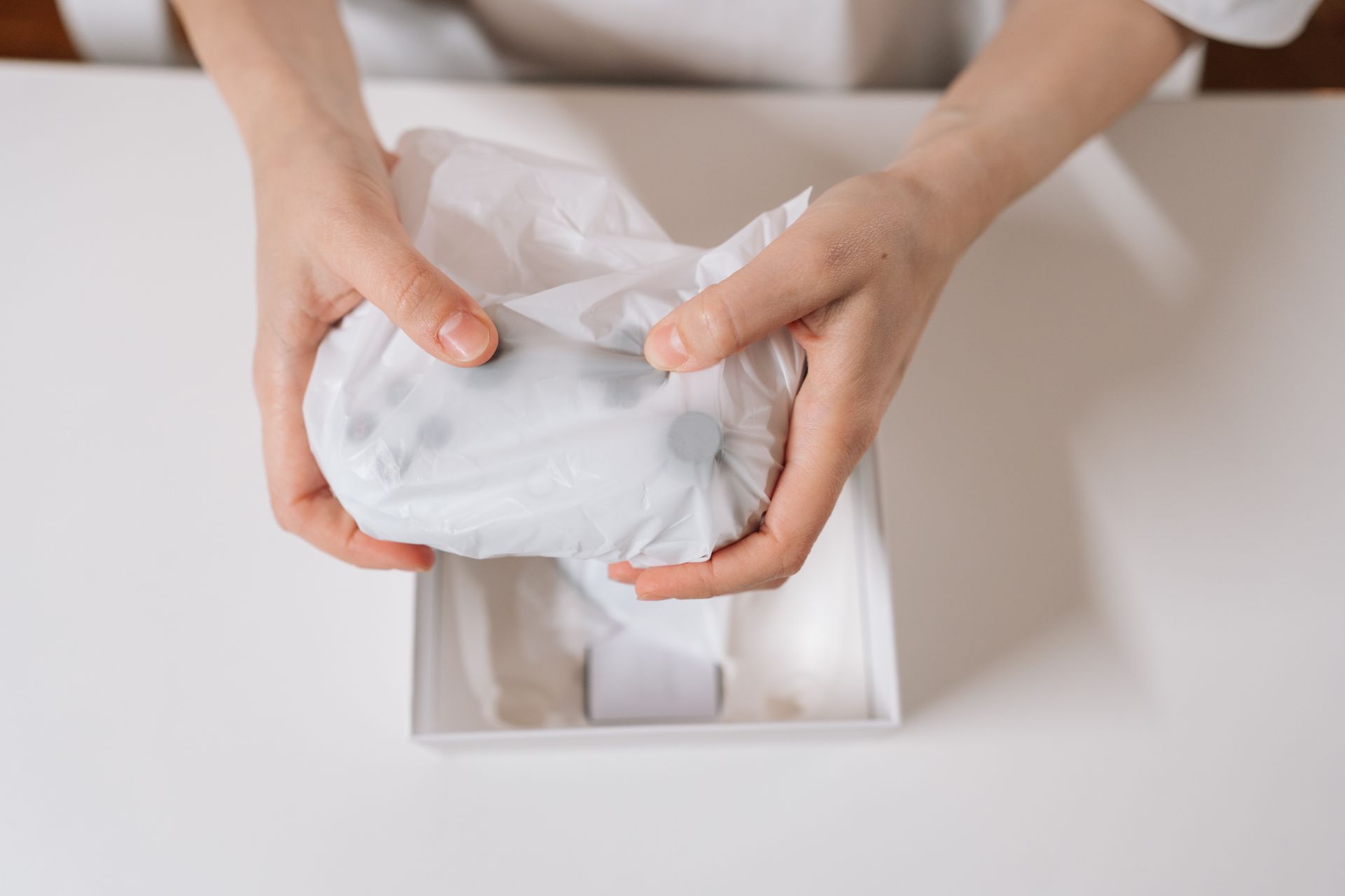 Hands unwrapping a white item from tissue paper in a box