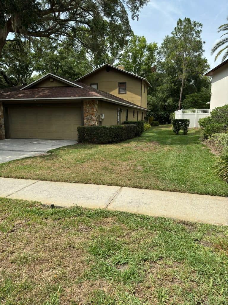 Suburban house with a two-car garage, front lawn, and sidewalk under trees