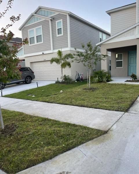 Suburban townhouse with two-story gray siding, driveway, sidewalk, and small front lawn at dusk