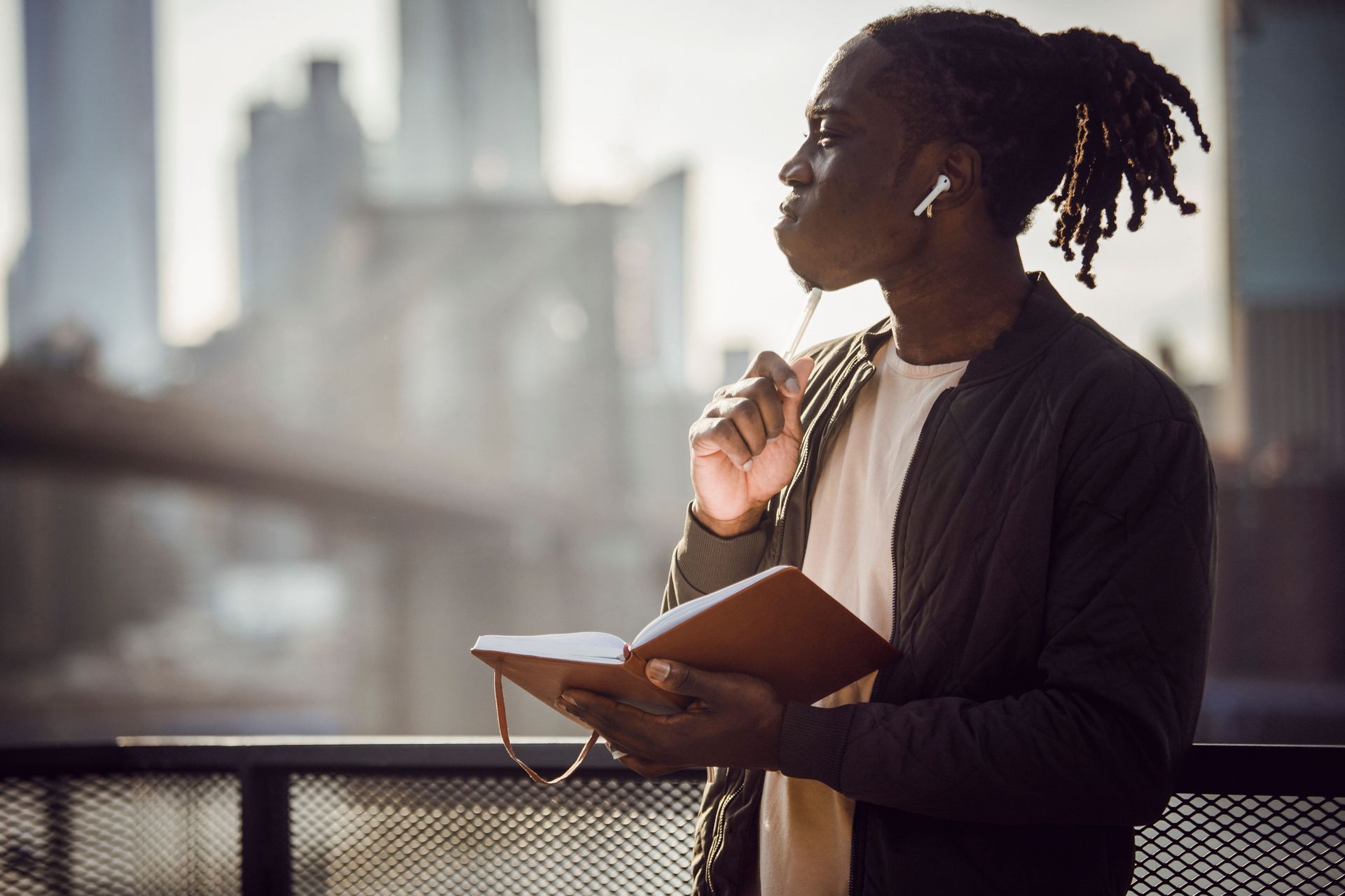 Person standing on a balcony reading a notebook with a city skyline blurred in the background