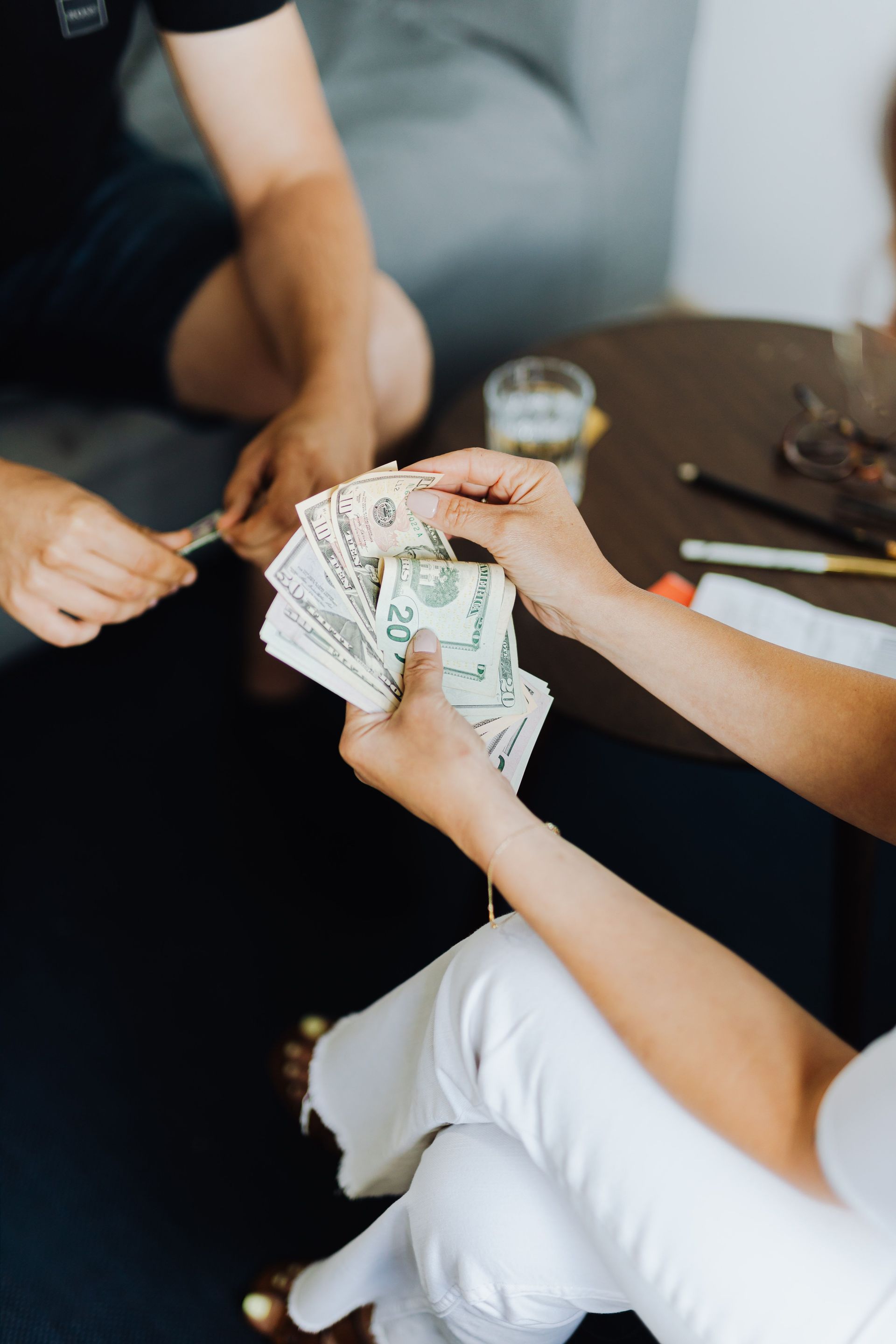 Hands counting cash at a table with drinks and papers nearby