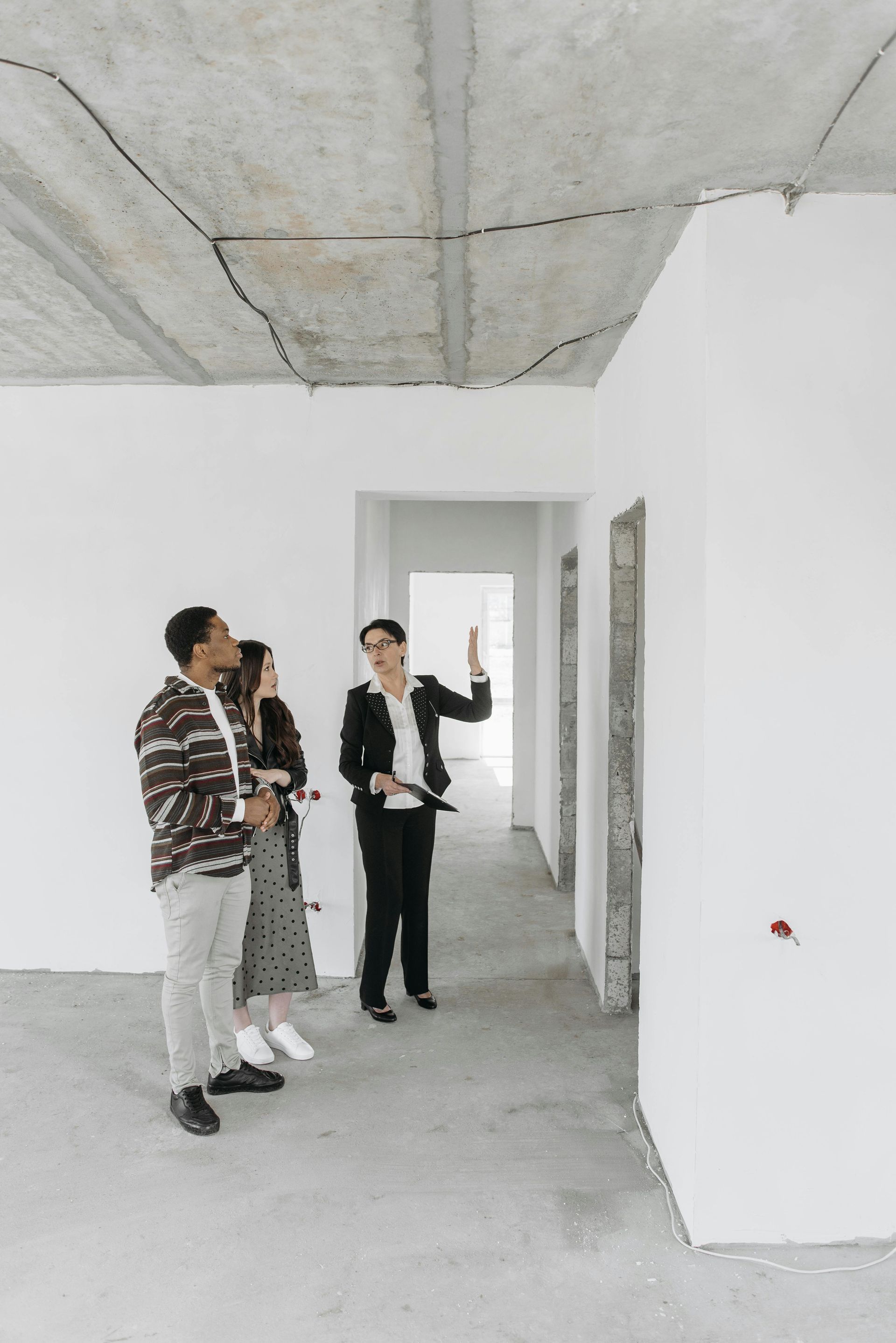 Three people stand in a bare room under construction, looking at the unfinished ceiling and walls.