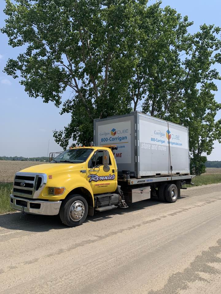 Yellow box truck parked on a rural road beside trees and fields