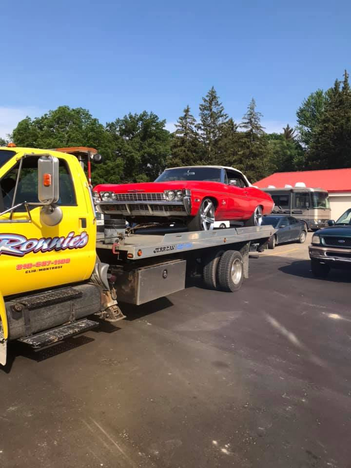 Red classic car on a flatbed tow truck in a parking lot on a sunny day