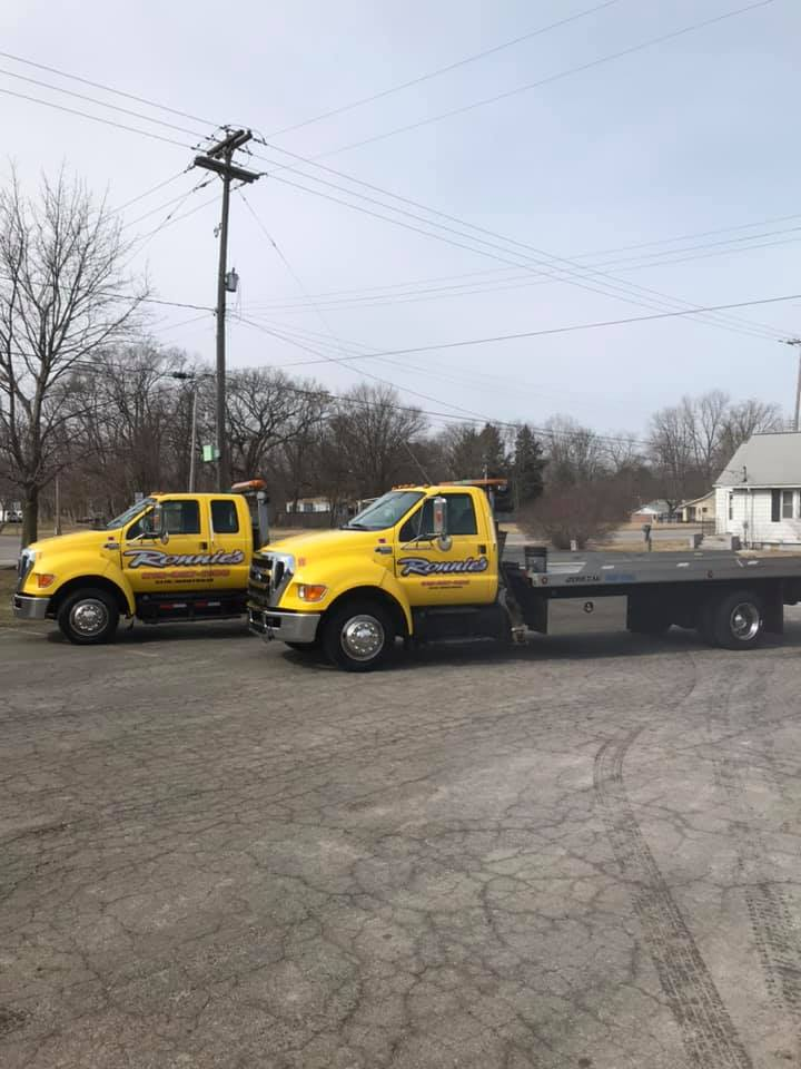 Two yellow tow trucks parked on a roadside with one hauling a flatbed trailer.