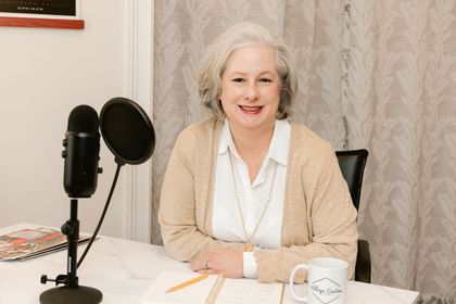Susannah Hodges, publisher, seated at a desk with a microphone, smiling in a home studio setting