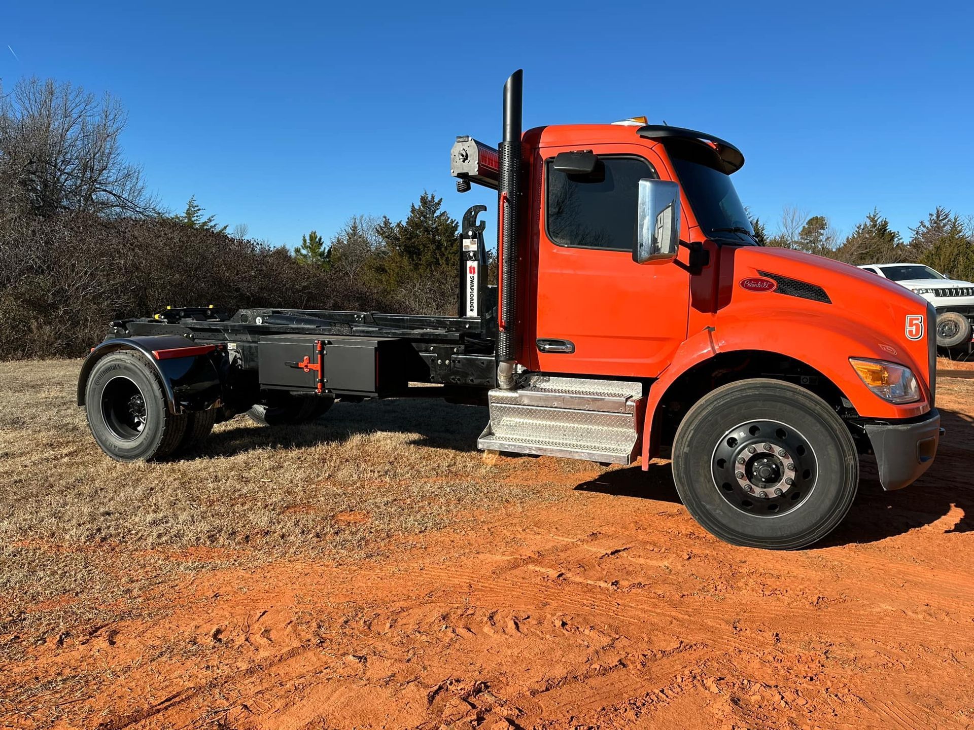 A red semi truck is parked in a dirt field.