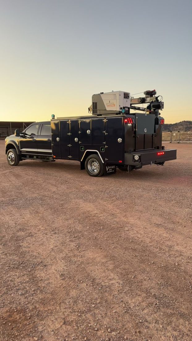 A black truck with a trailer attached to it is parked in a dirt field.