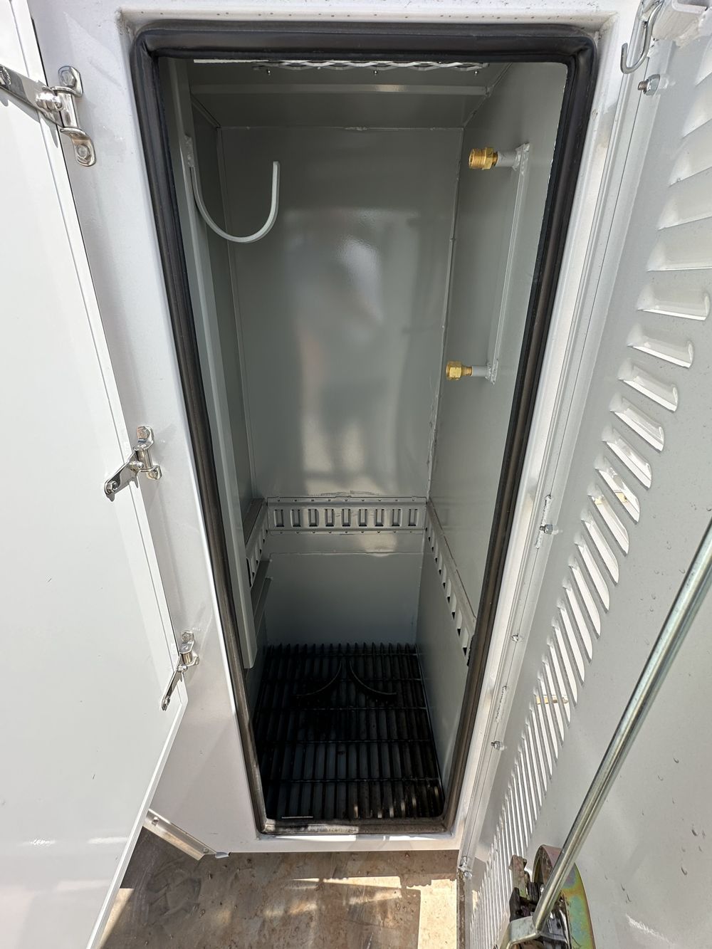 A white cabinet with the door open and a black mat on the floor.