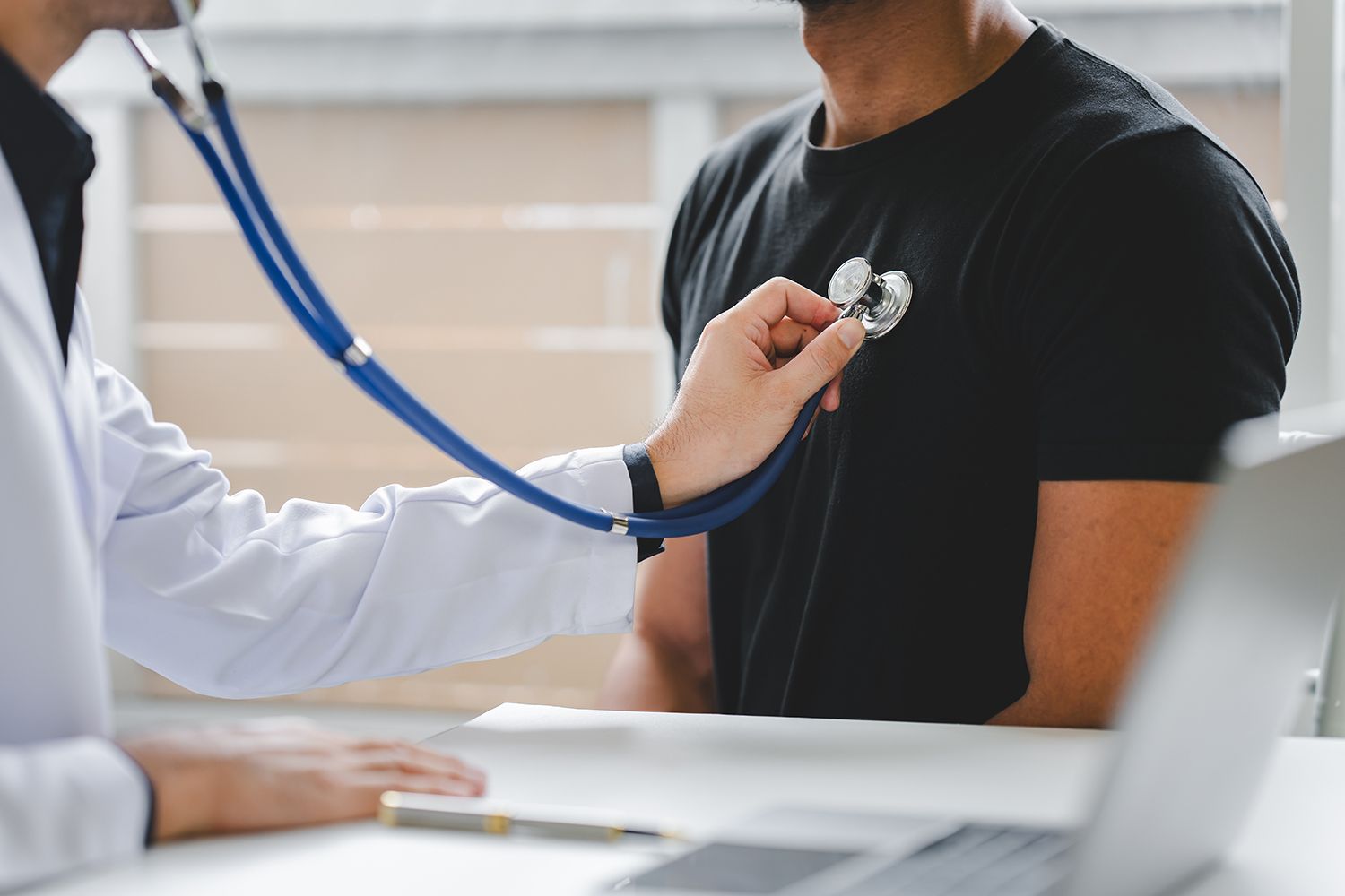Doctor using a stethoscope to examine a seated patient in a clinic office Doctor using a stethoscope to examine a seated patient in a clinic office