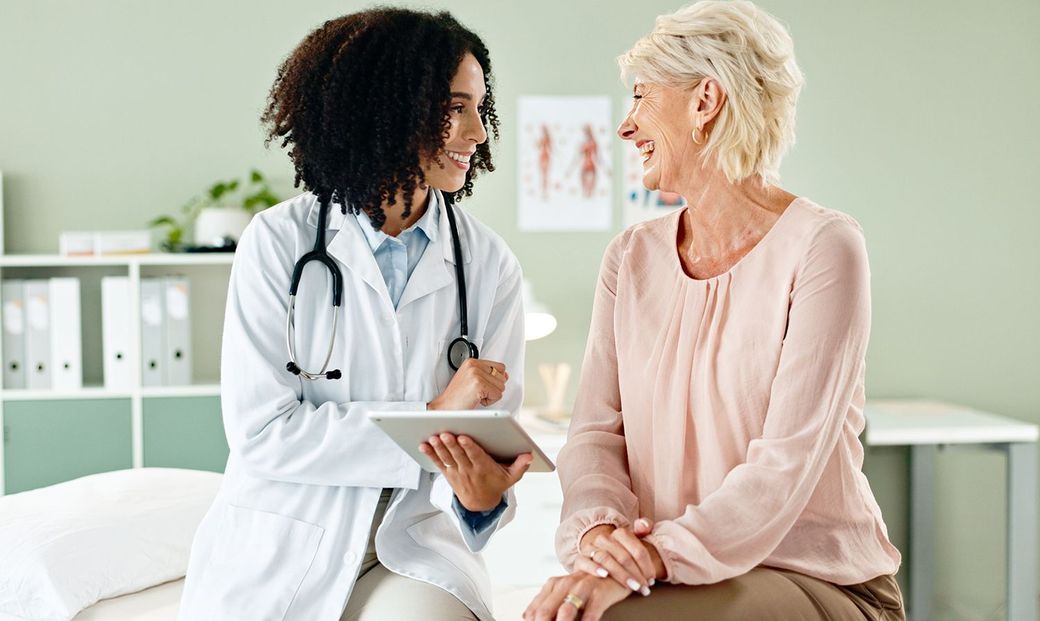 Doctor consulting with a patient in a bright clinic, holding a tablet while seated together and talking. Doctor consulting with a patient in a bright clinic, holding a tablet while seated together and talking.