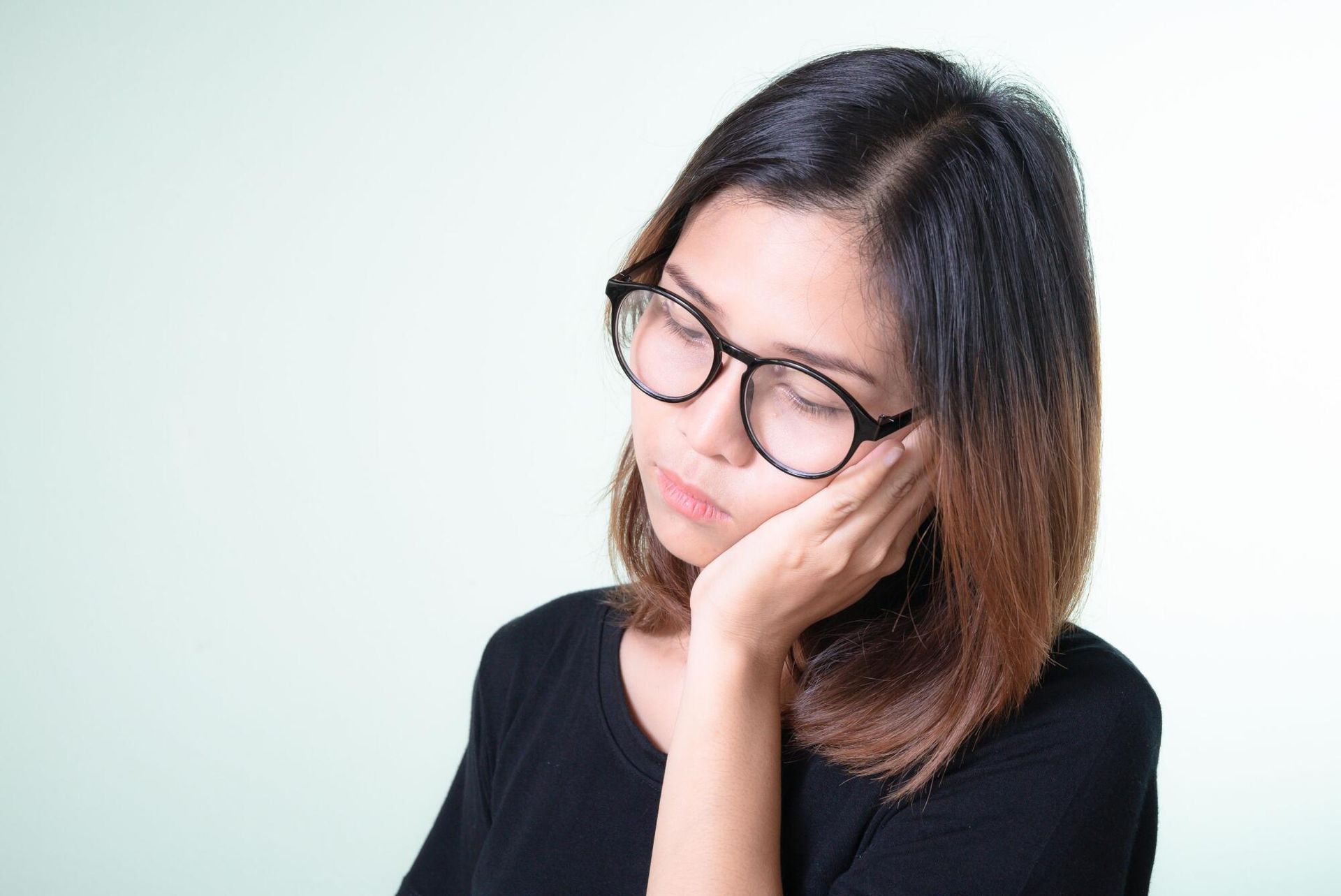 Woman with glasses resting her head on her hand against a light background