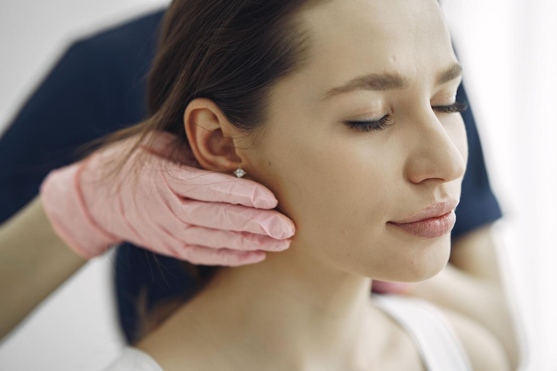 Gloved hands gently examining a woman’s ear during a medical consultation
