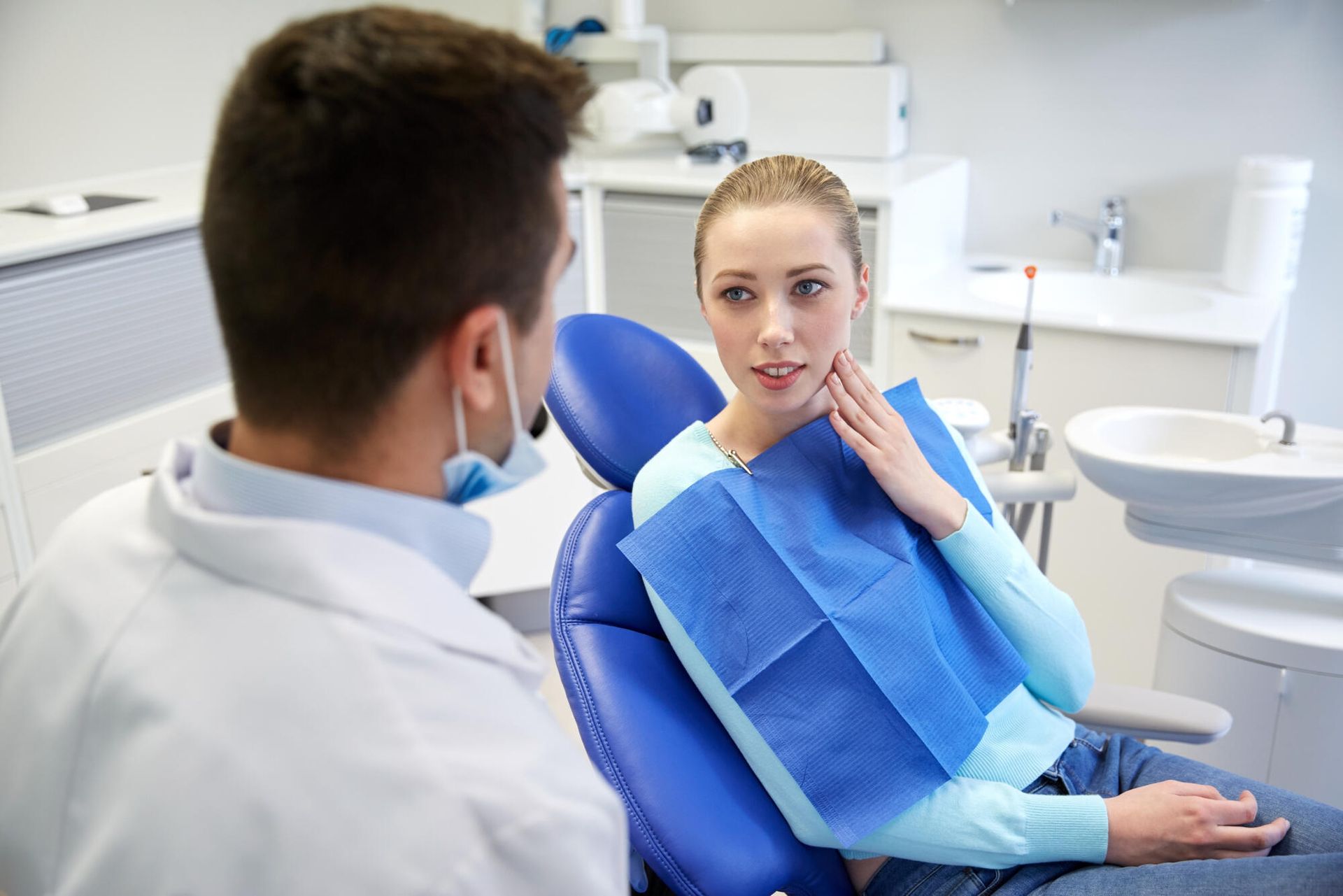 Dentist consulting with a patient in a bright dental clinic; patient wears a blue bib.