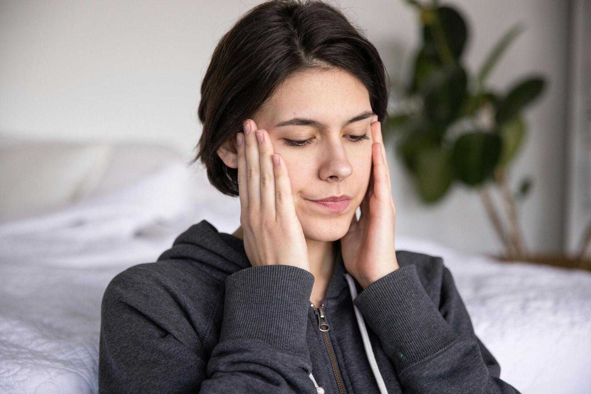Person holding their face with a pained expression on a bed, in a bedroom