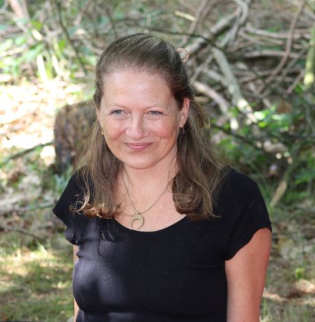 Vrouw in zwarte blouse lacht buiten met bomen op de achtergrond.