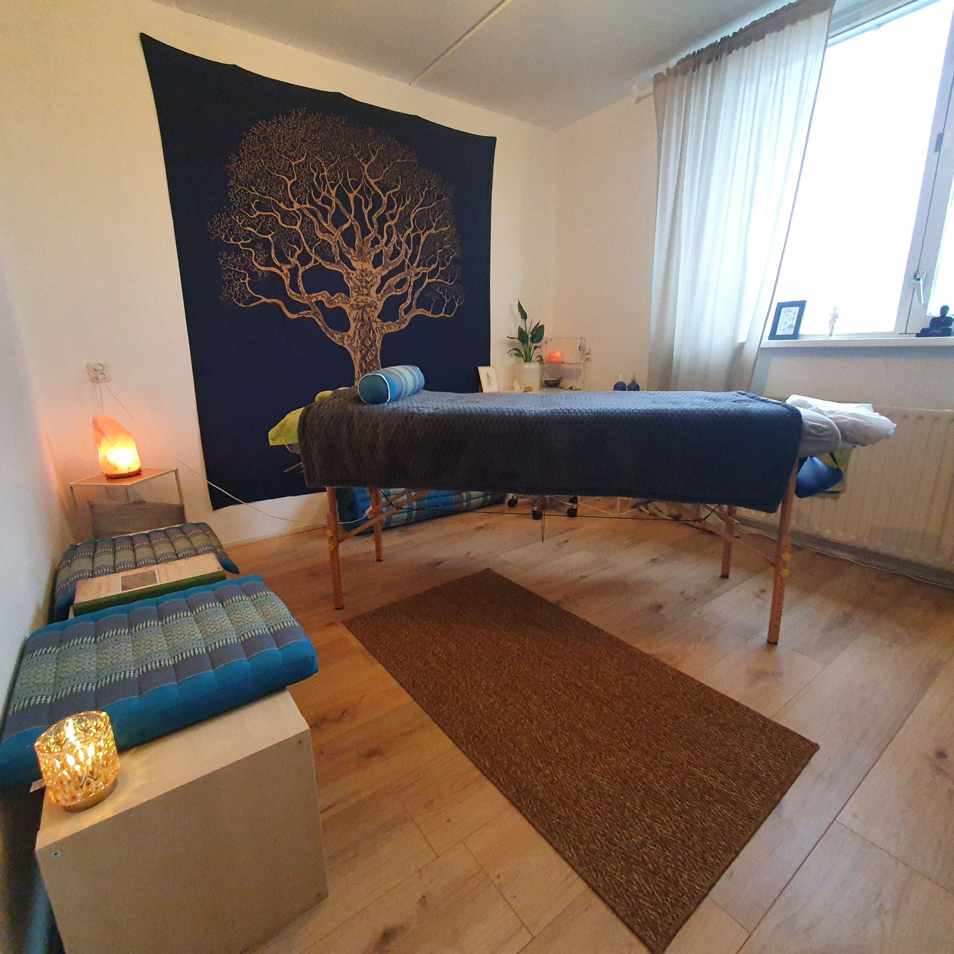 Massageruimte met massagetafel, vloerkleed en wandtapijt.
