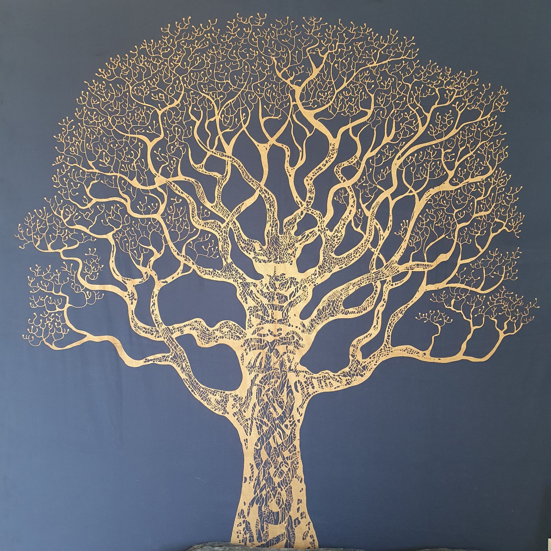 Gouden boommuurschildering op een donkerblauwe muur met een vertakte kruin en een gestructureerde stam.