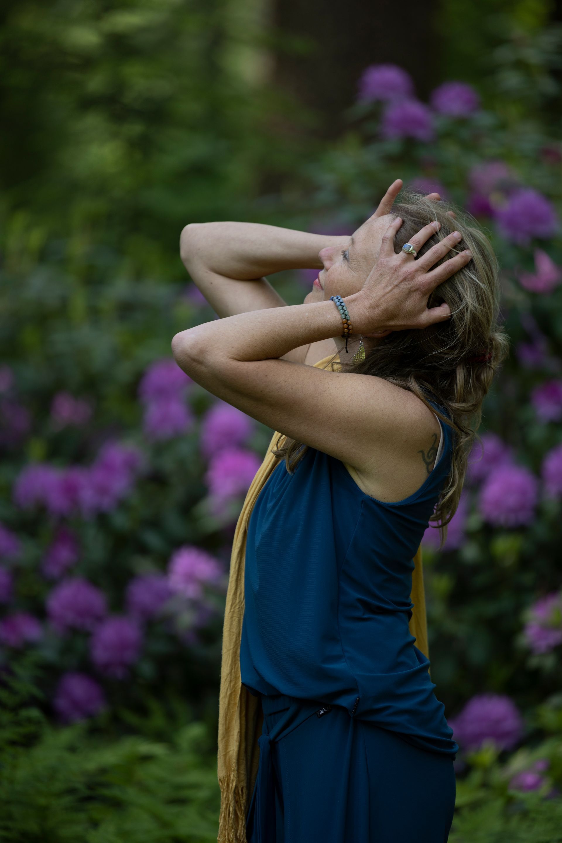 Een vrouw in een blauwe jurk staat voor paarse bloemen.