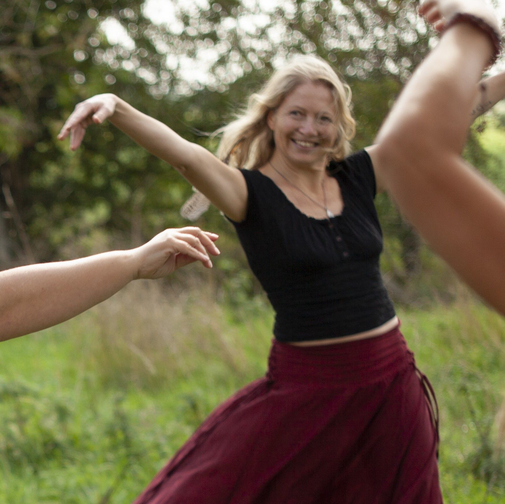 Een vrouw danst buiten in een zwarte top en bordeauxrode rok, lachend met haar armen omhoog.