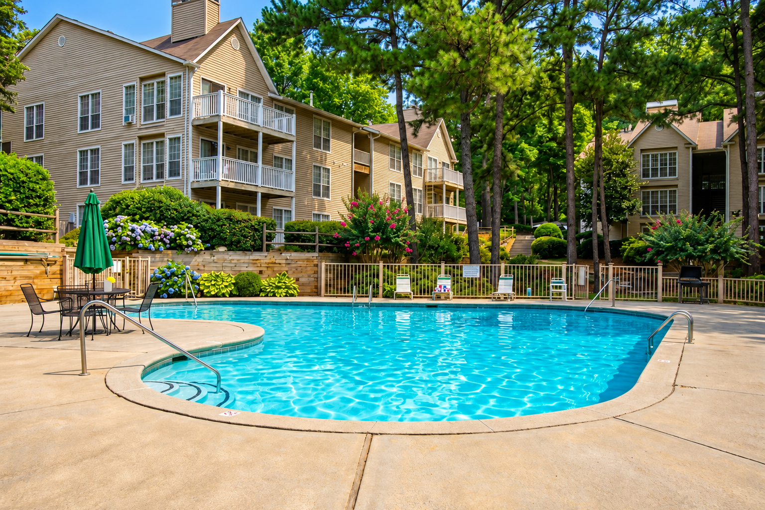 Outdoor apartment pool with turquoise water, patio chairs, and stone buildings surrounded by trees.