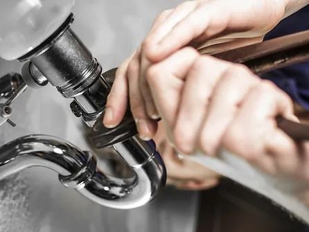 A plumber is fixing a sink pipe with a wrench.