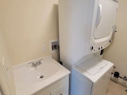 A bathroom with a sink , washer and dryer stacked on top of each other.