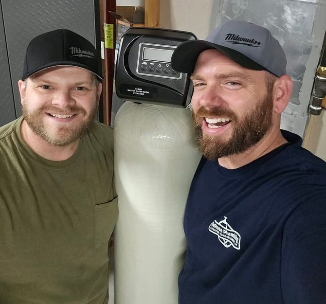 Two men are posing for a picture in front of a water filter.
