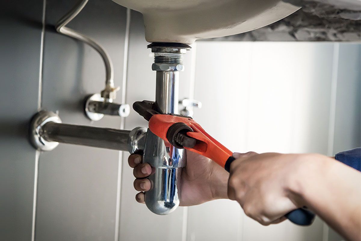 A plumber is fixing a sink pipe with a wrench.