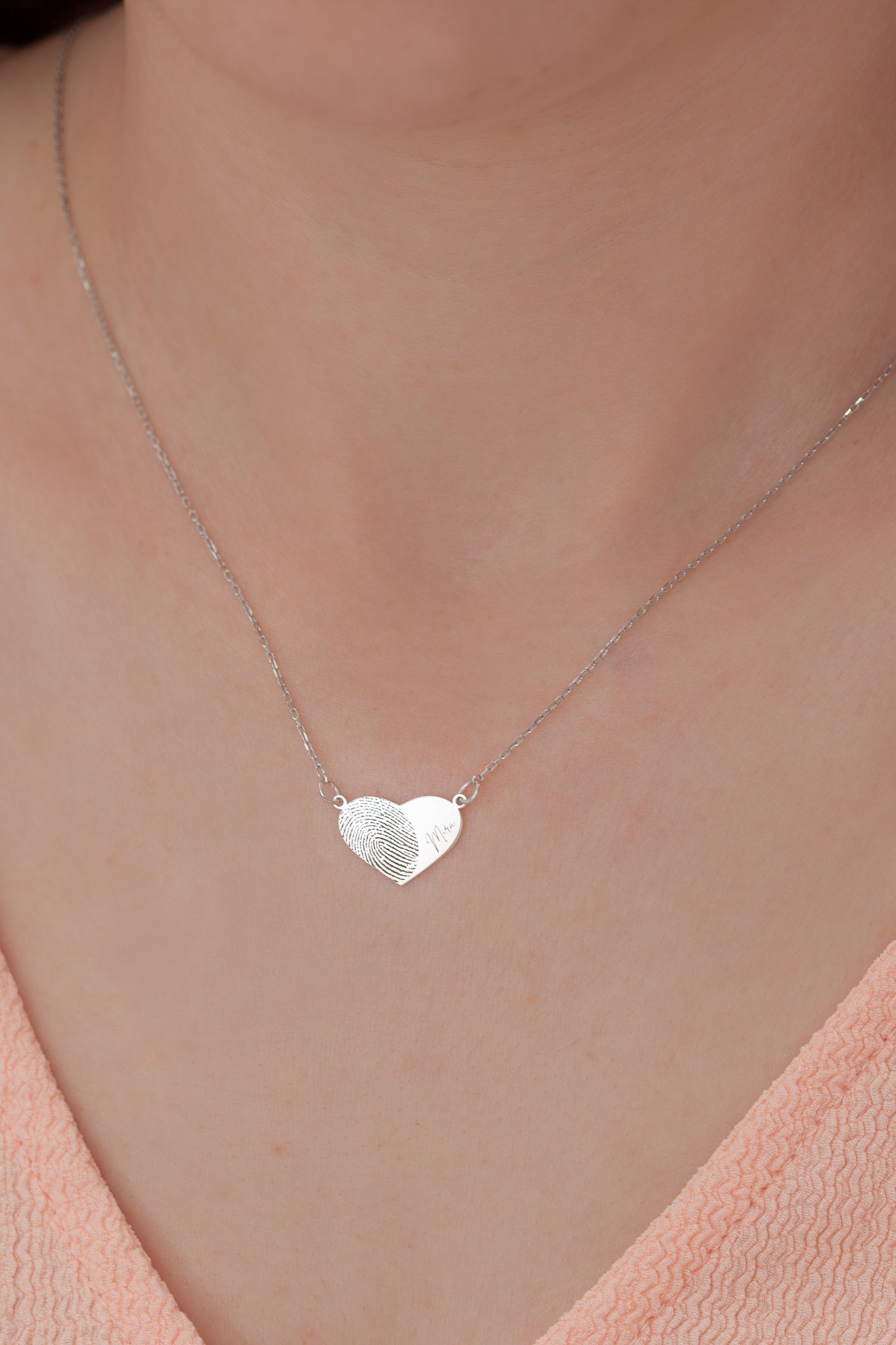 Silver heart pendant necklace on a person's neck with a peach-colored top.
