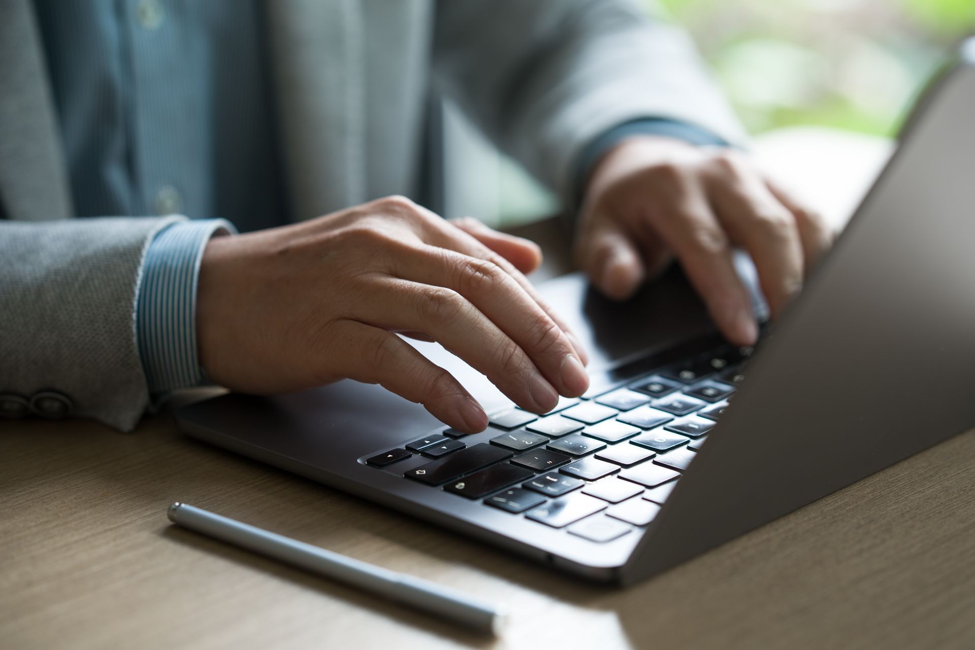 Hands typing on a laptop at a wooden desk, with a pen beside it.
