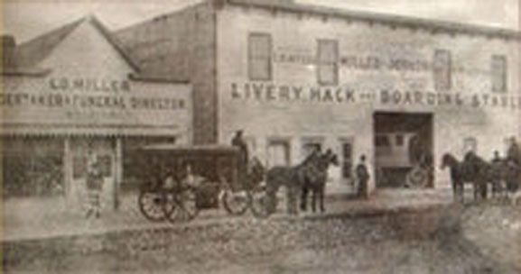 Vintage black-and-white street scene of a livery stable and hack boarding house with horse-drawn carriages outside