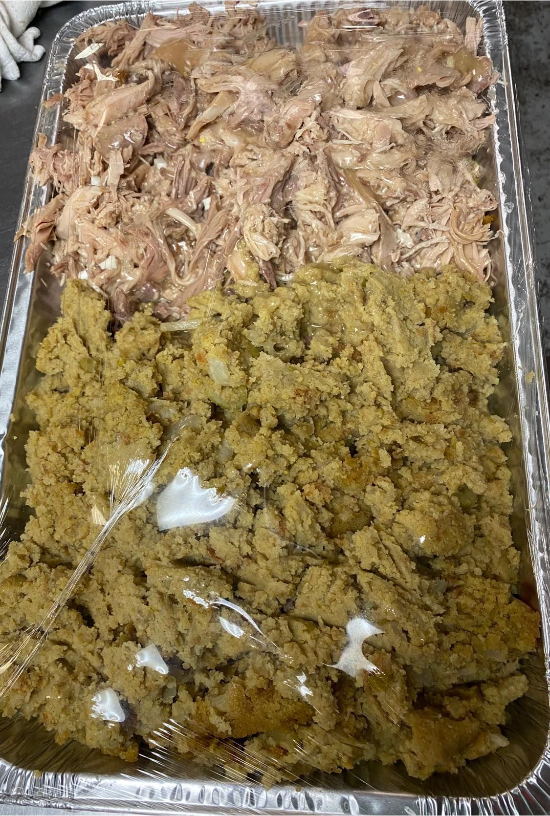 A foil catering tray divided between shredded pulled pork and savory bread stuffing.