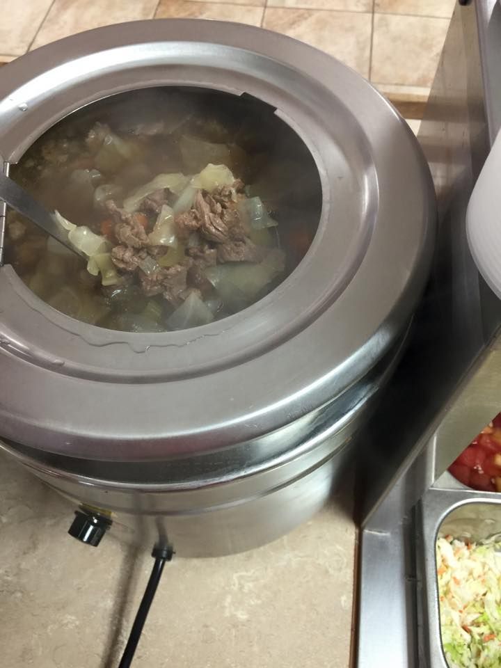 A metal soup warmer filled with beef and cabbage stew, next to a container of shredded vegetables on a counter.