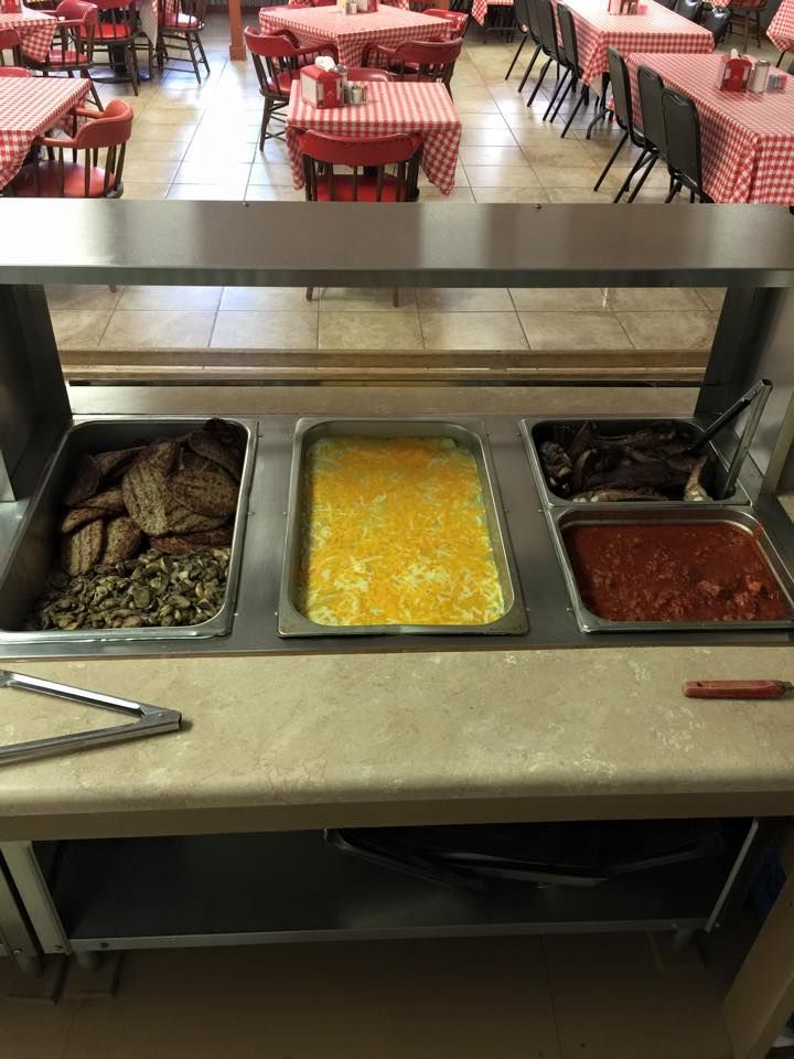 A buffet station featuring a metal counter with three pans of food, located in a restaurant with checkered tables.