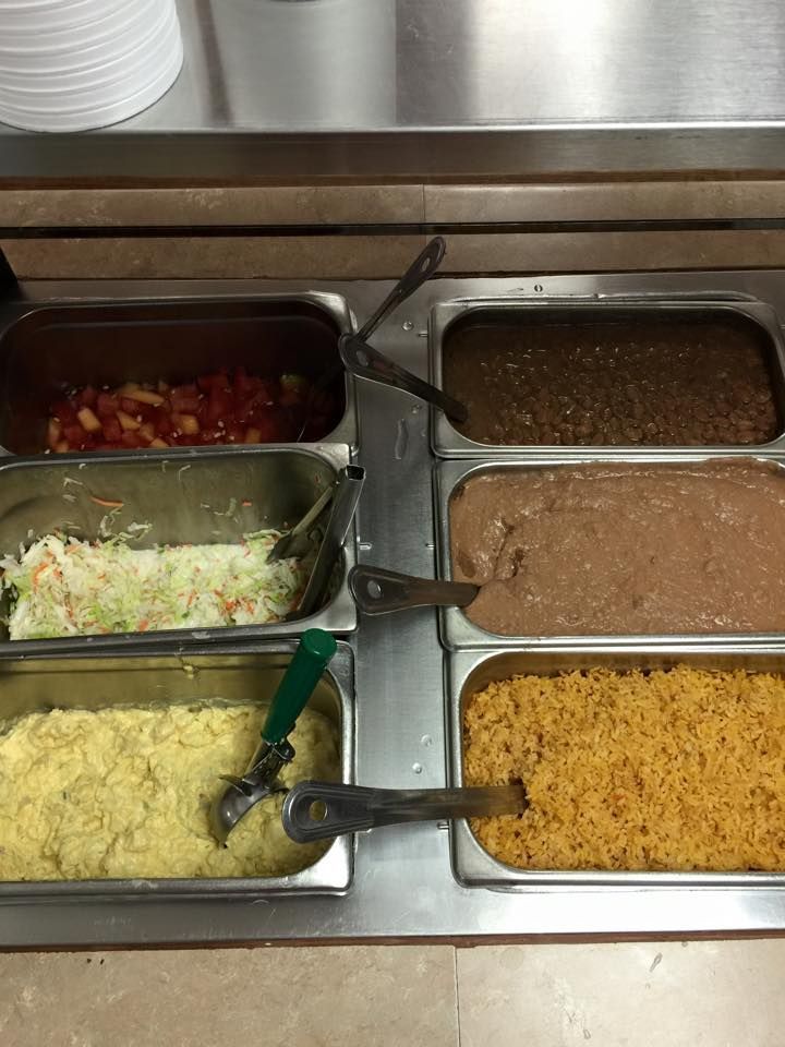 A buffet station with six metal food containers holding various ingredients, including rice, beans, and salad.