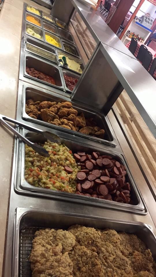 A metal buffet line filled with various hot foods, including fried chicken, sliced sausage, and side dishes.