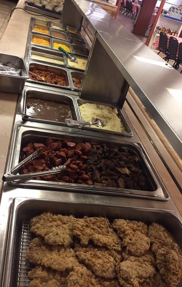 A buffet serving line featuring metal pans filled with fried chicken, sausage, side dishes, and sauces.