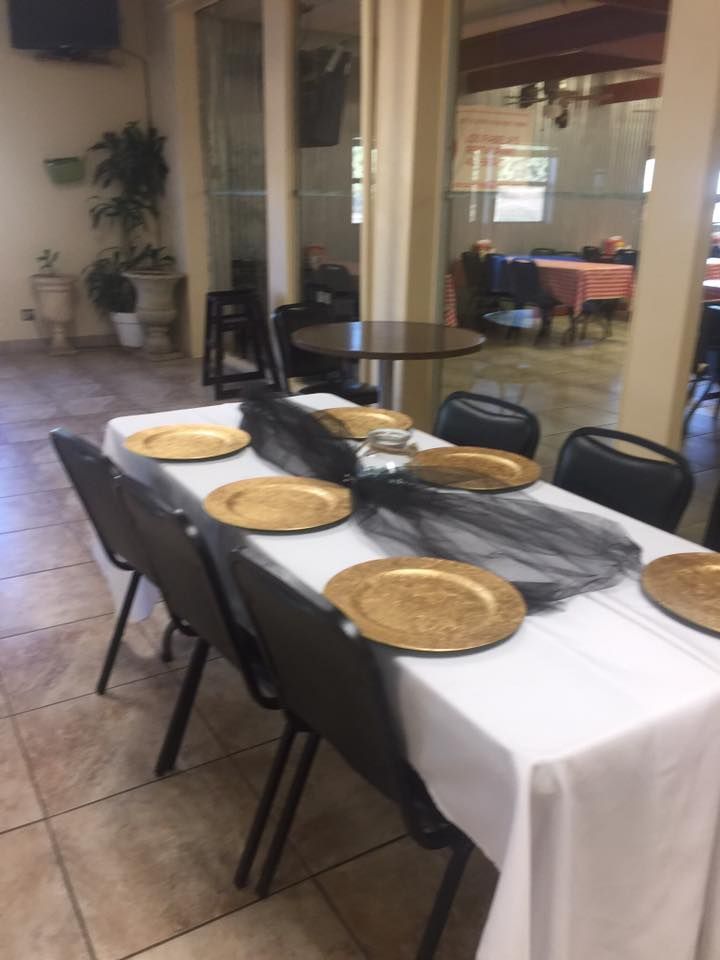A banquet table set with white tablecloths, black tulle runners, and gold chargers in a dining room with tiled floors.