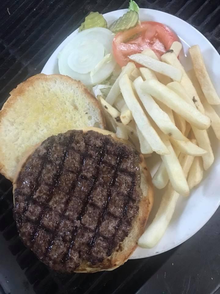 A hamburger patty on a bun next to a serving of french fries, with onion, tomato, and pickles on a white plate.