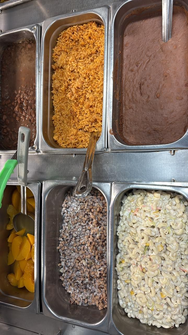 A metal food service tray with six compartments holding yellow rice, refried beans, peach slices, wild rice, and pasta salad.