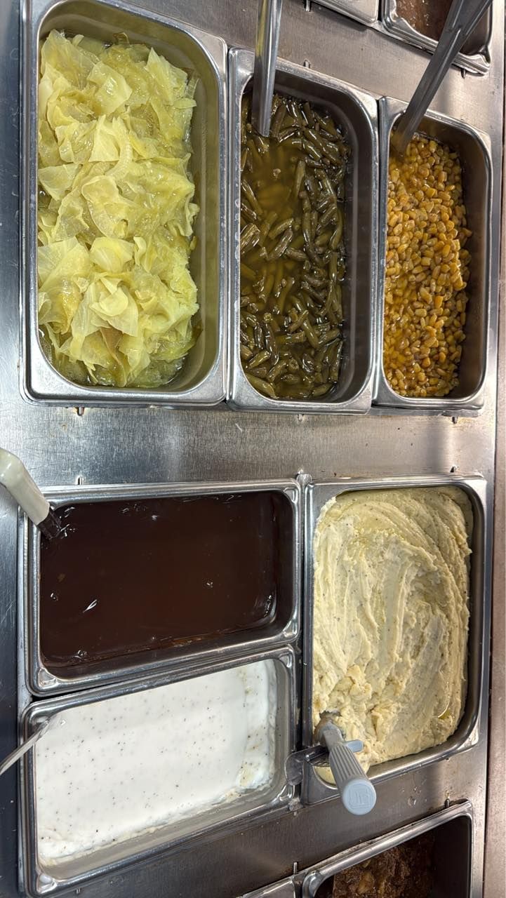 A stainless steel food prep station with various sides, including mashed potatoes, gravy, green beans, and corn.
