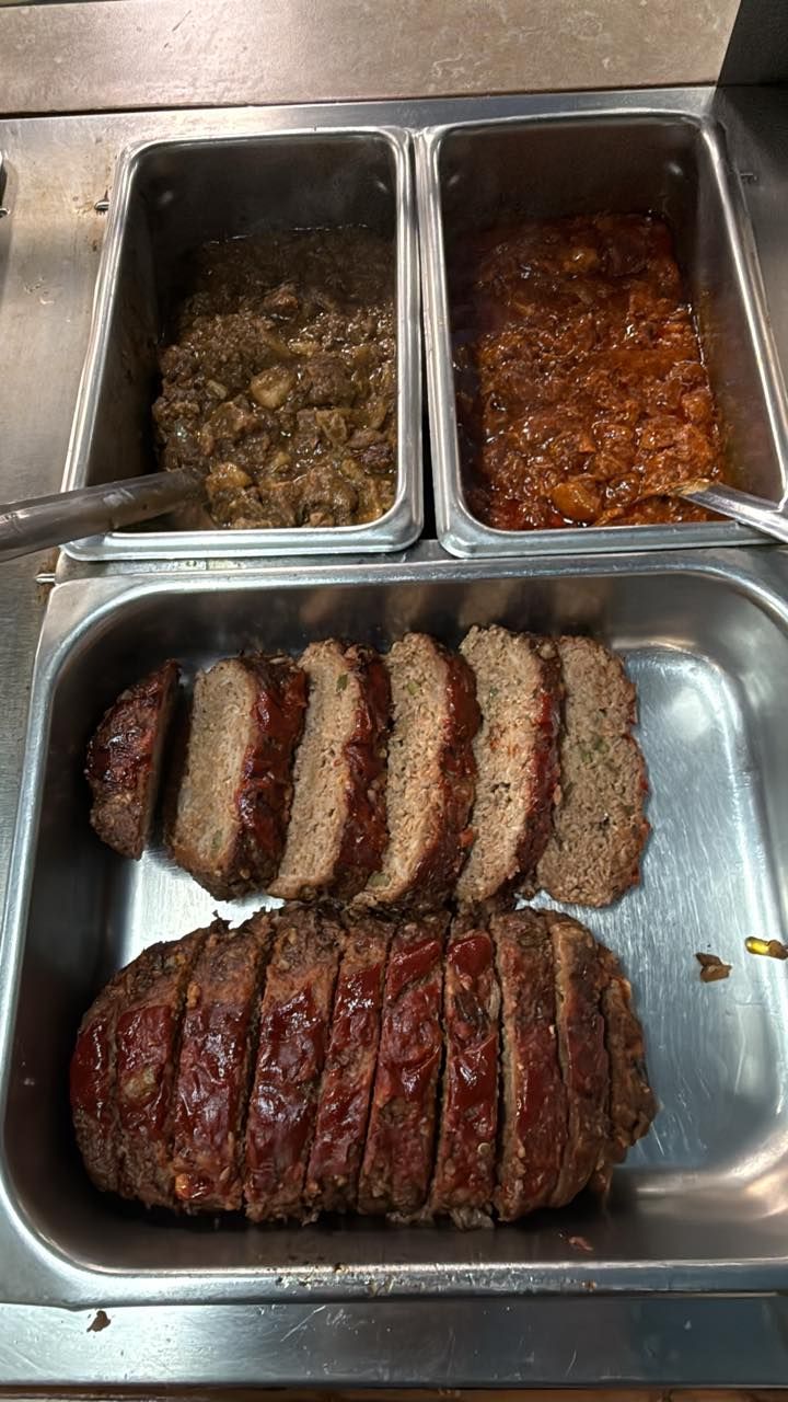 A cafeteria food warmer containing two pans of meatloaf slices and two smaller pans of gravy or side dishes.