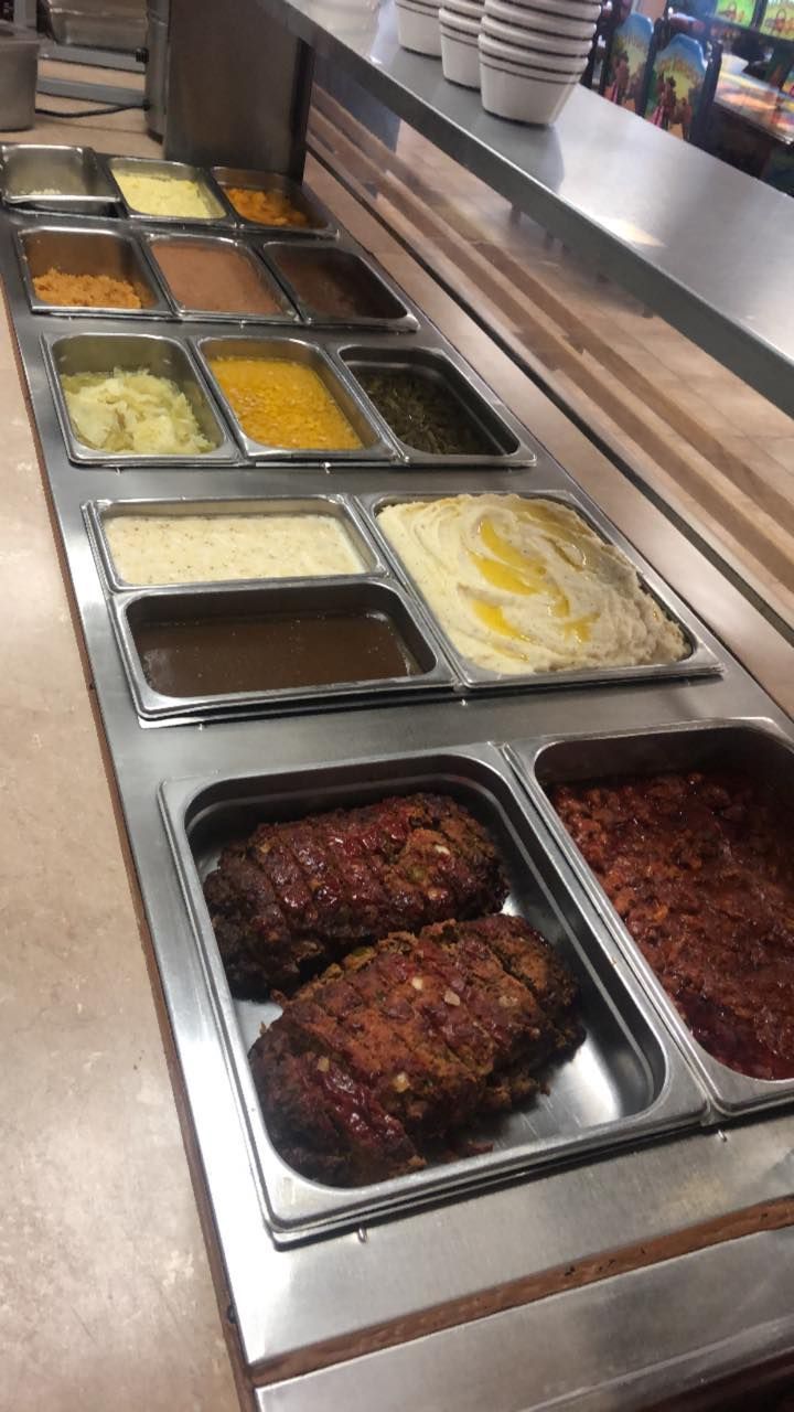 A cafeteria food buffet line featuring various warm dishes, including meatloaf, mashed potatoes, gravy, and side items.