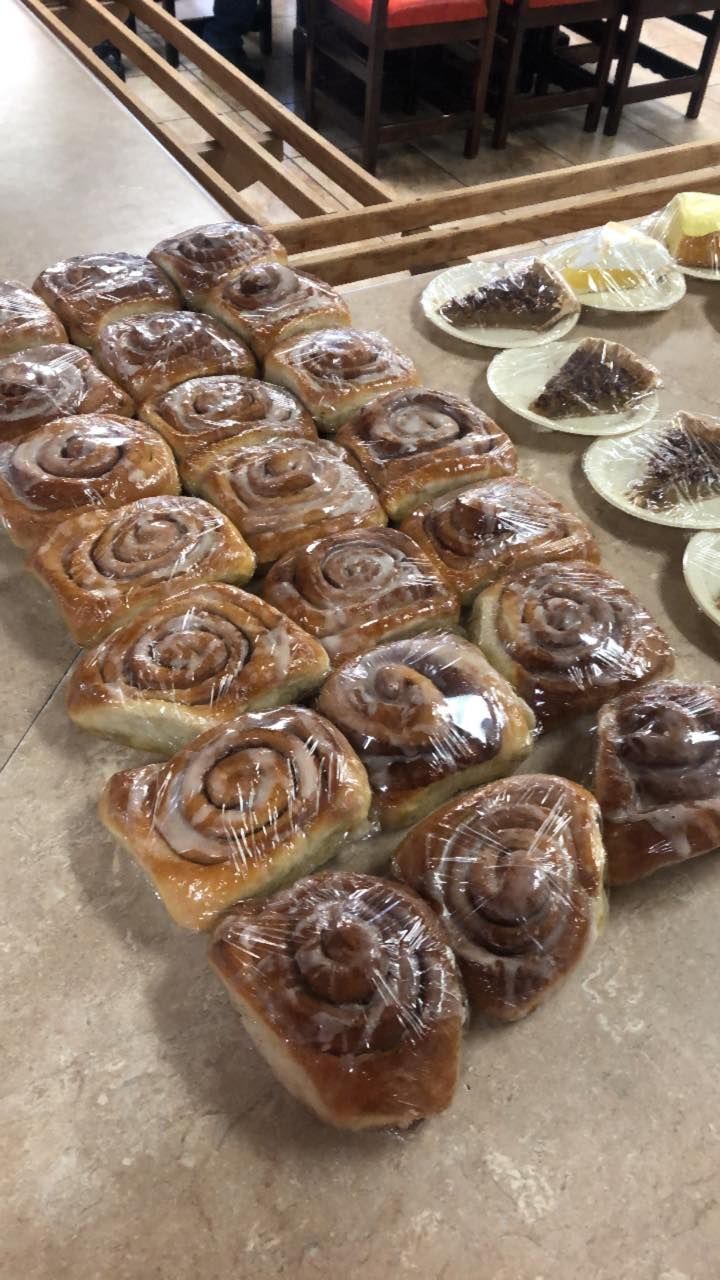 A tray of glazed cinnamon rolls arranged in rows next to small plates with portions of pastry on a counter.
