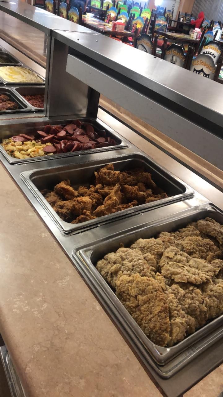 A buffet serving line featuring metal pans filled with breaded chicken, fried food, and sliced sausage.
