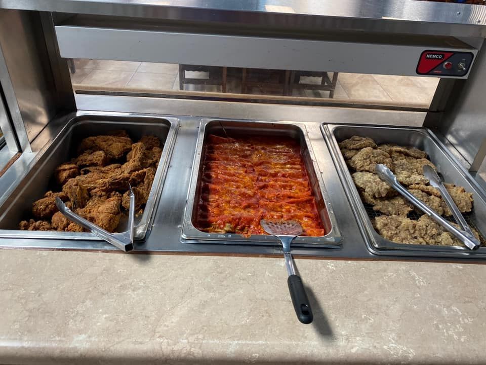 A buffet warmer holding three metal pans containing fried chicken, red sauced pasta, and breaded cutlets with utensils.