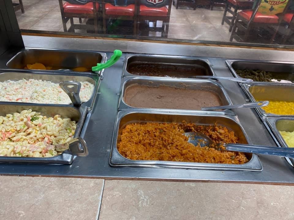 A restaurant buffet station with metal trays containing various side dishes, including rice, beans, pasta, and salads.