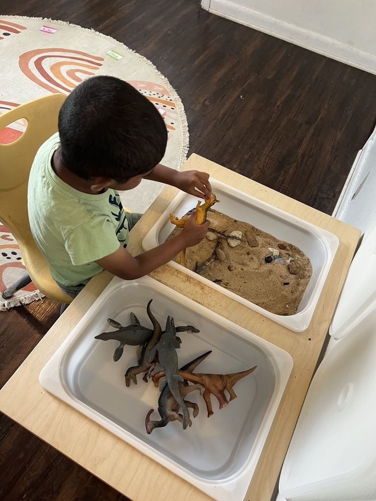Child playing with toy animals and sand in a white tray at a table indoors